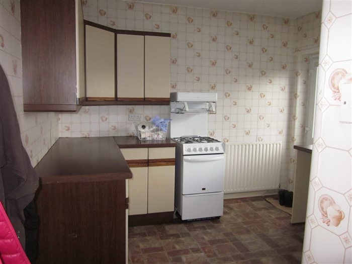 Kitchen before: brown units, patterned wallpaper and vinyl floor